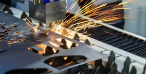 Fiber laser cutting machine cutting through an aluminum sheet with a bright beam and sparks.