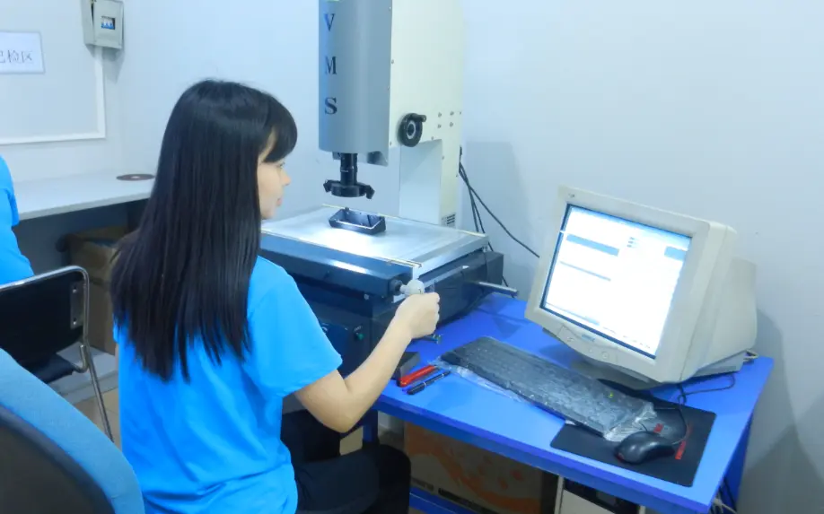 A technician performs a precision measurement on a zamak casting part using a Video Measuring System (VMS) in the quality inspection area.